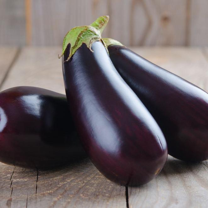Three glossy purple eggplants on a wooden board