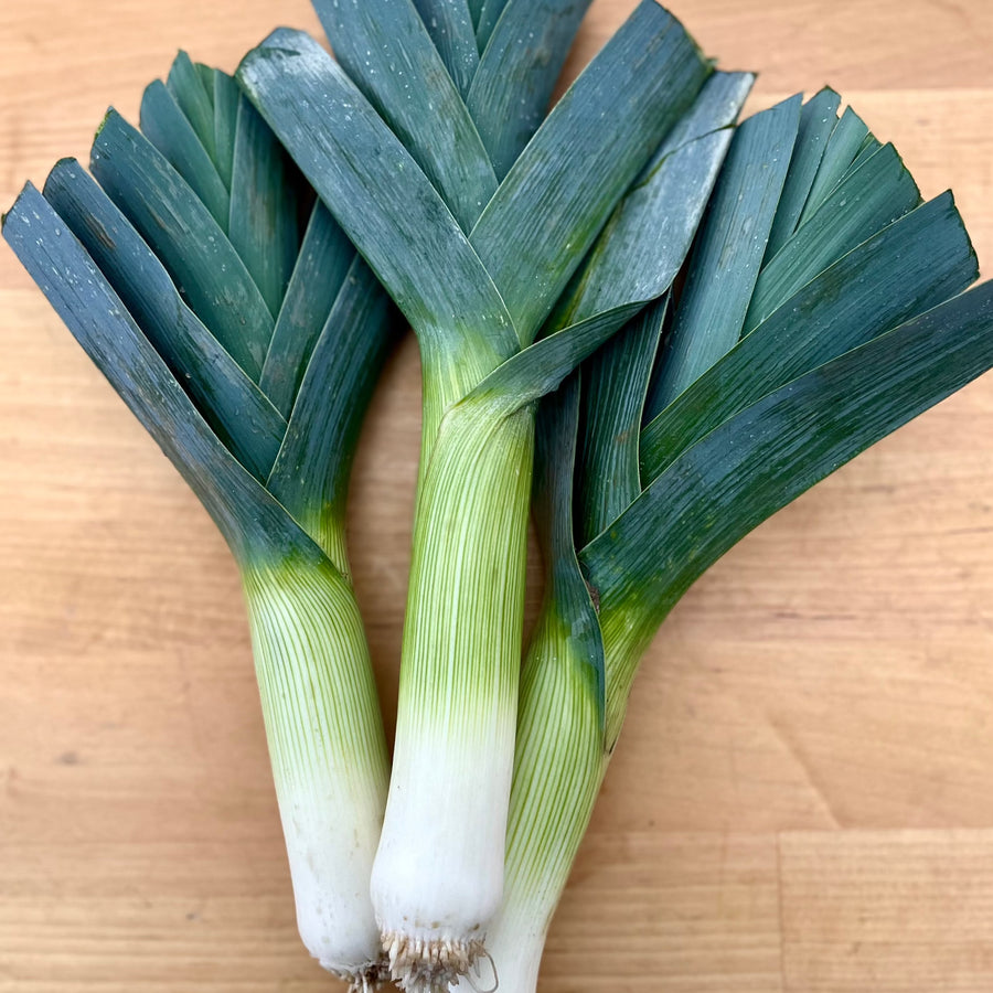 Three whole leeks with dark green tops on a wooden board